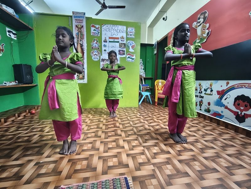 Students in green and pink practice costume holding namaskaram in a Mayura Natyalaya class