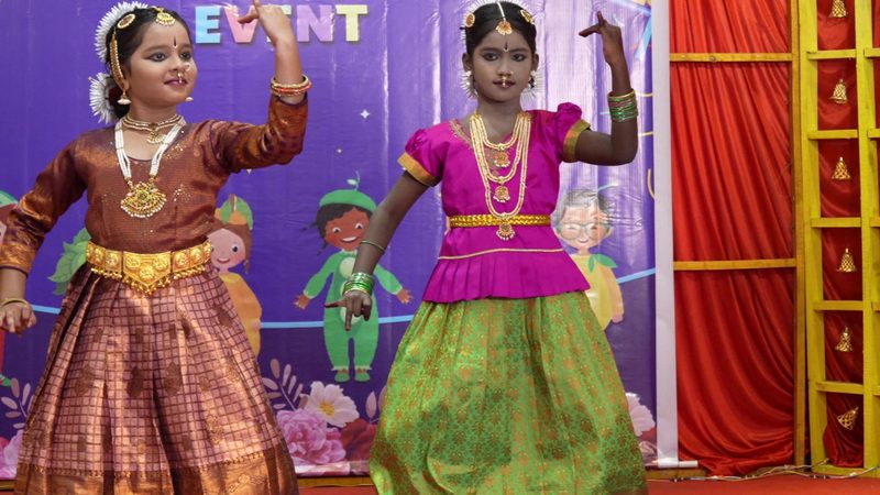 Two young dancers smiling mid-performance in Bharatanatyam costume