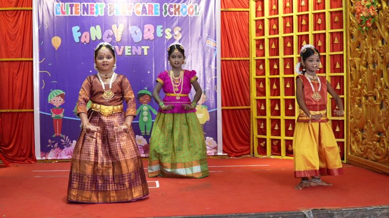 Three students performing Bharatanatyam on a red stage at Elite Nest Play School