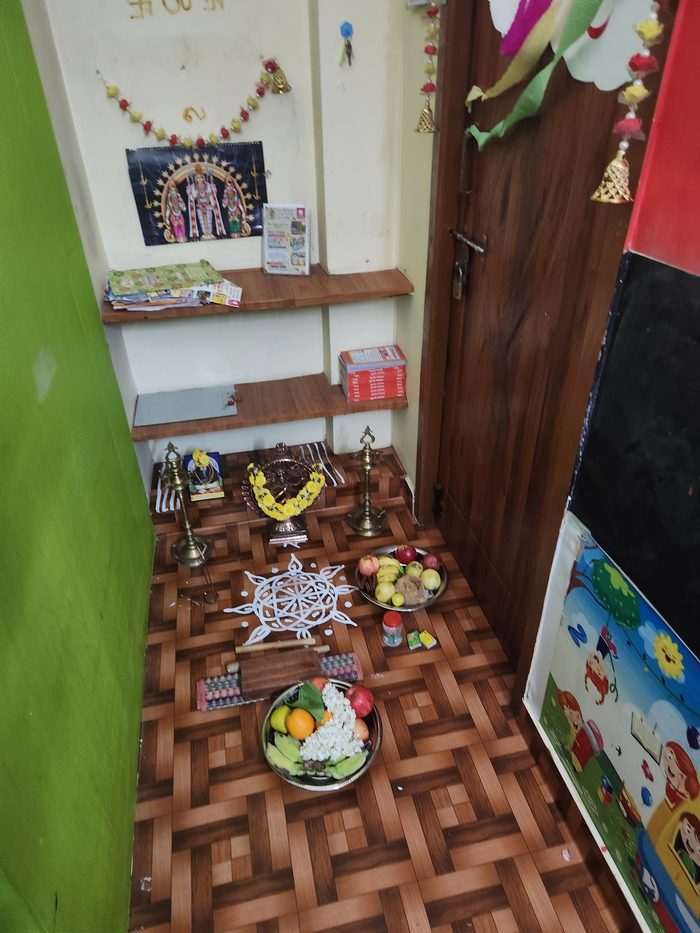 A pooja arrangement with lamps, flowers and fruit before the first classes